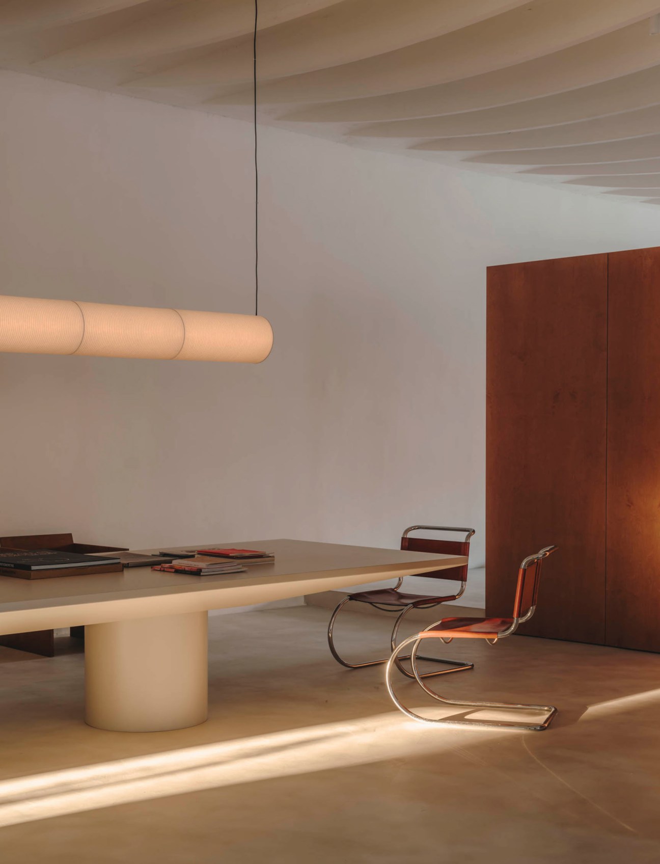 Modern dining room with beige cylindrical table, cantilever chair, and warm pendant lighting