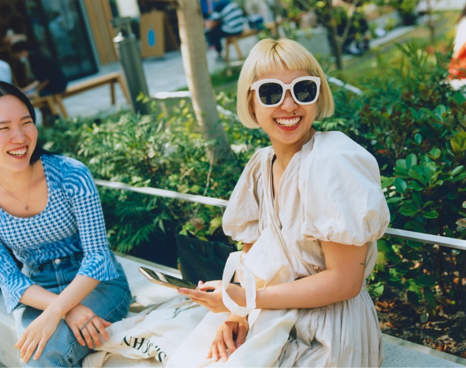 Two women smiling and relaxing on bench seating in Kitaya Park, Tokyo, surrounded by green plants.
