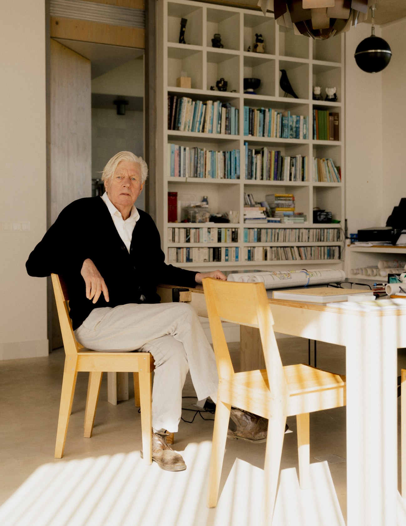 Piet Oudolf sitting at a wooden table in his home office with built-in bookshelves