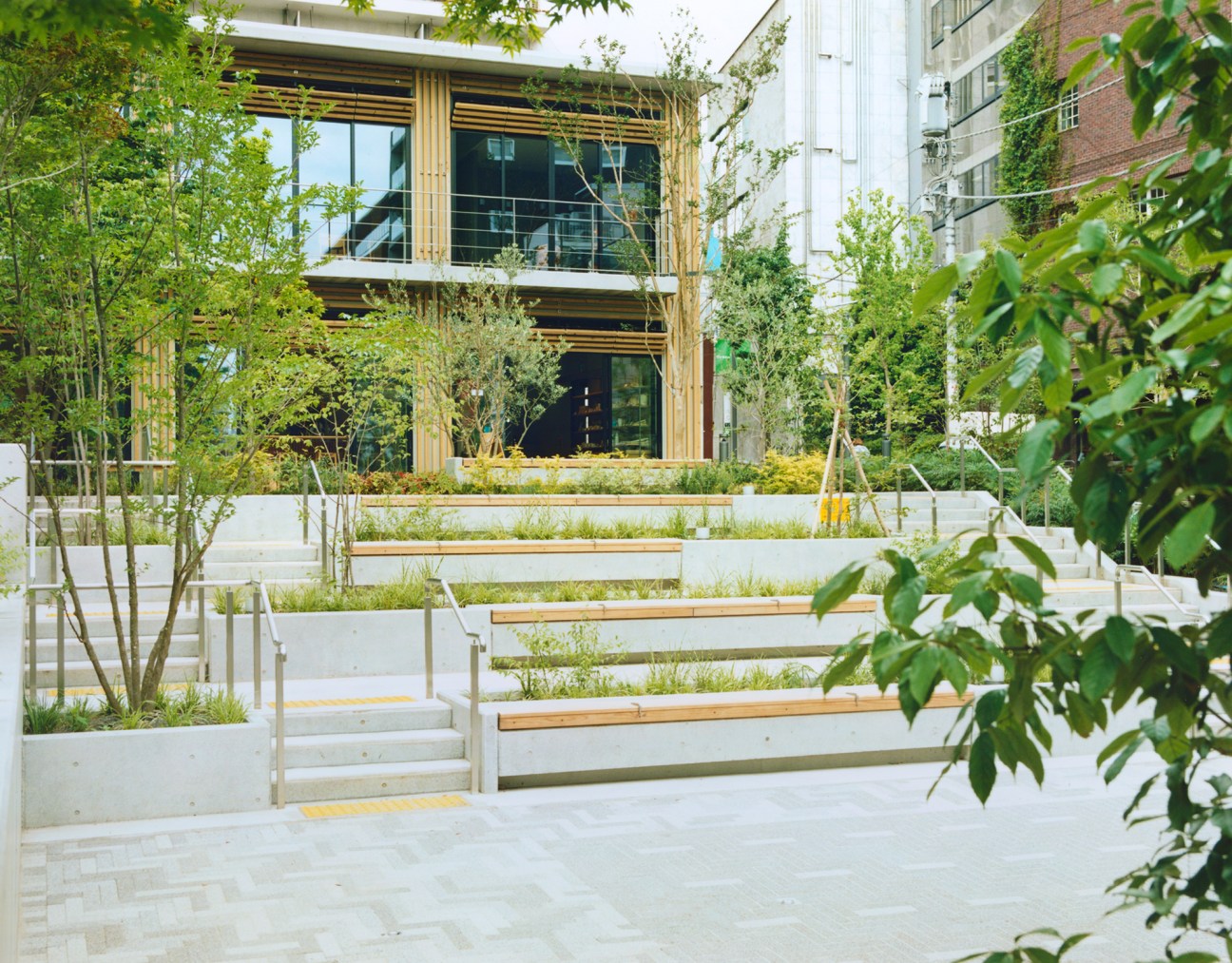 Kitaya Park in Tokyo features tiered white planters with wooden bench seating and young trees surrounding a modern building with wooden cladding.