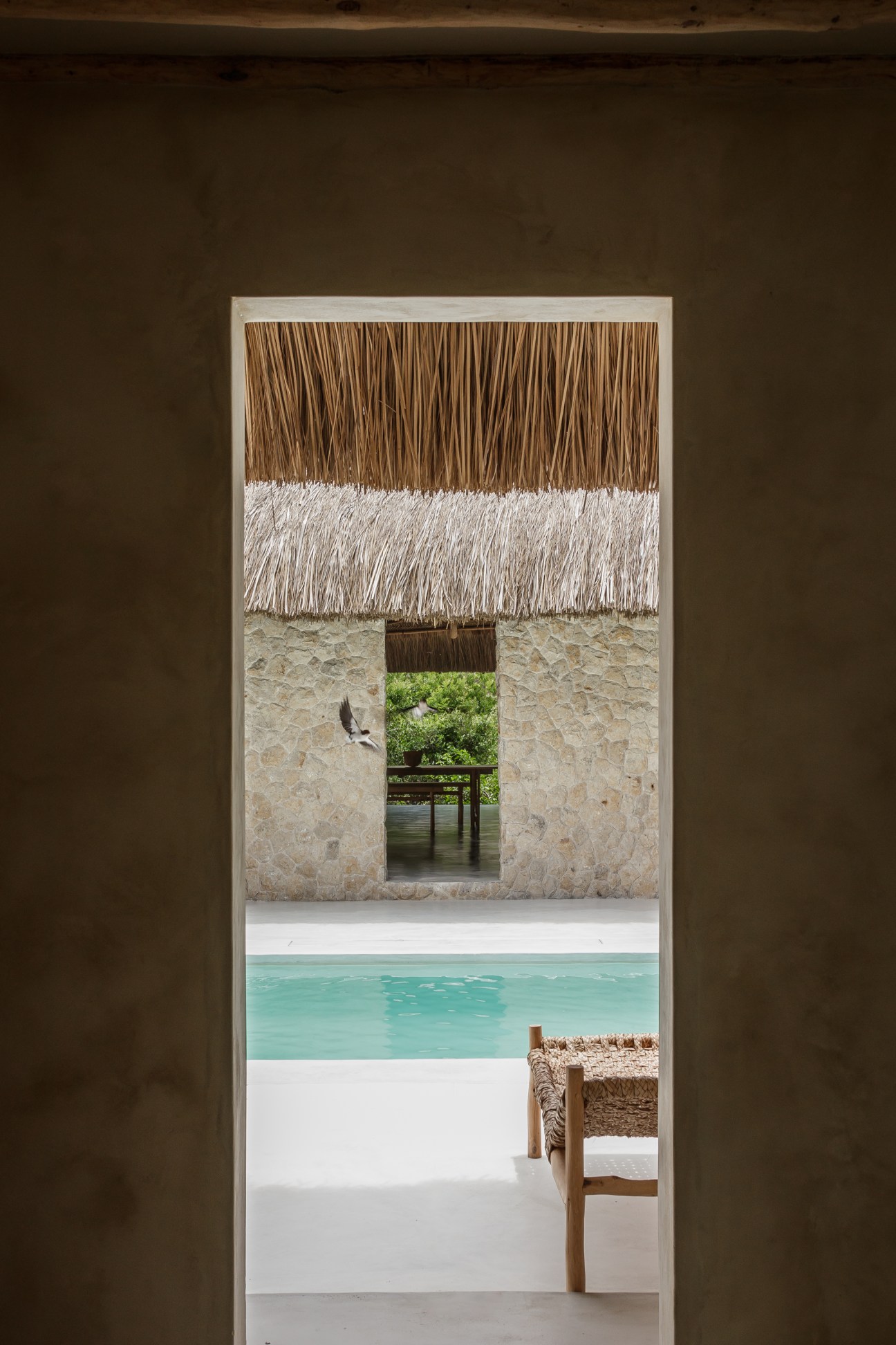 View through doorway showing thatched roof pavilion, turquoise pool, and wooden chair at Sussurro lodge