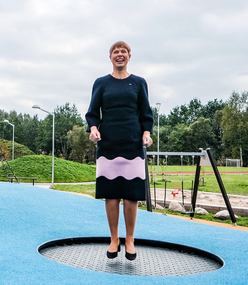 Woman in dark dress with pink stripe standing on circular trampoline in outdoor playground area