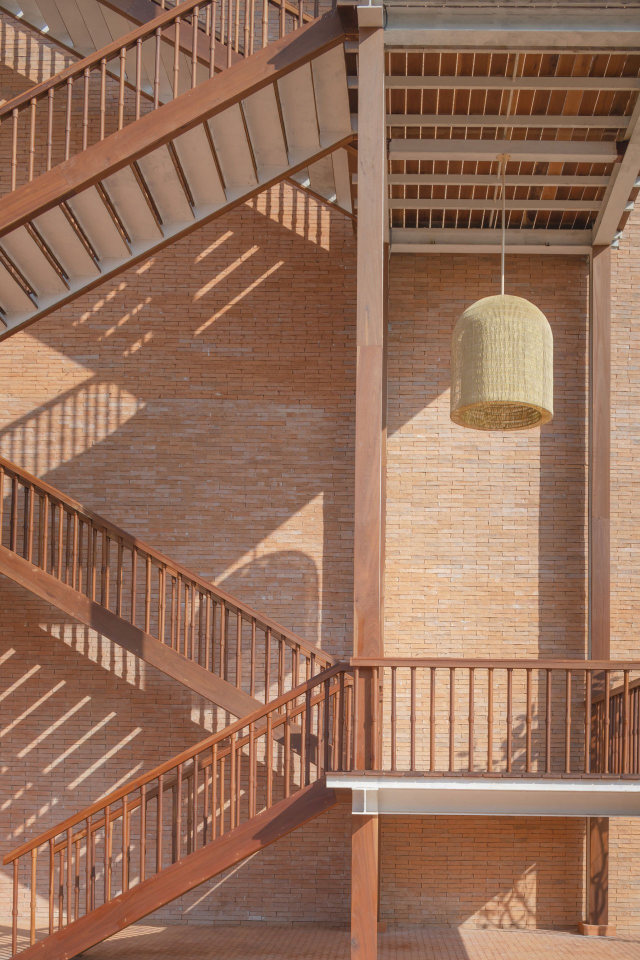 Interior staircase with orange brick walls, wooden railings, and a woven pendant light at Central Ayutthaya shopping centre.
