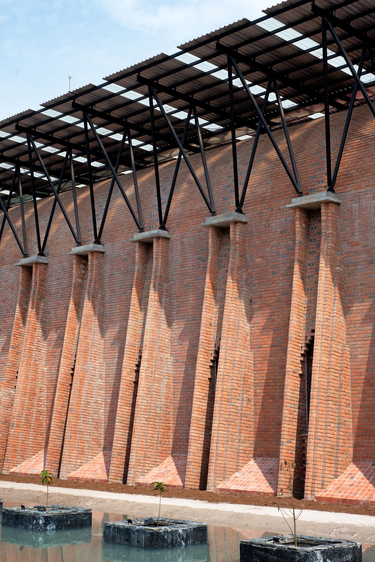 Brick building with distinctive angular buttresses and metal roof structure in Uganda by Localworks