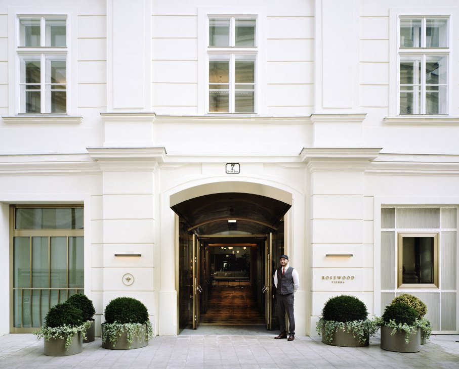 Elegant hotel entrance with white neoclassical facade, doorman in uniform, and Rosewood Vienna signage
