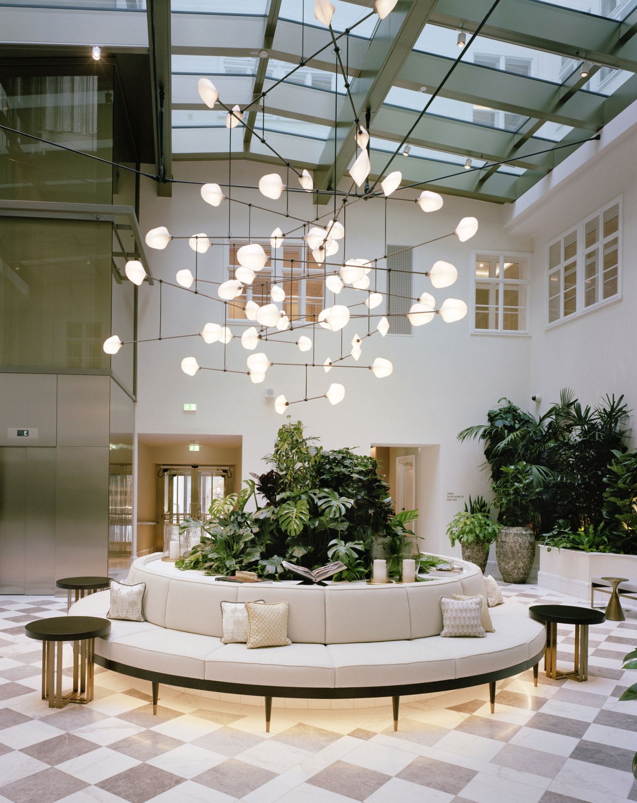 Modern hotel lobby atrium with geometric chandelier, circular seating area, and glass ceiling at Rosewood Vienna
