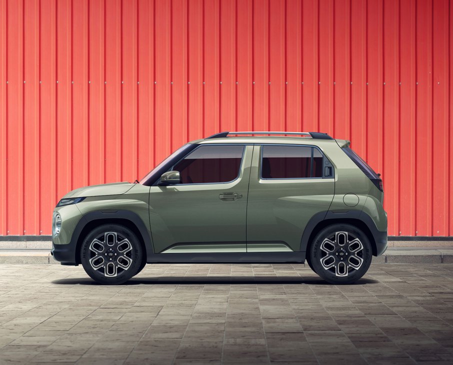 Olive green Hyundai Casper compact SUV with roof rack parked against red corrugated metal wall
