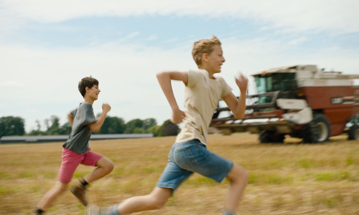 Two young boys running across a field with a truck in the background