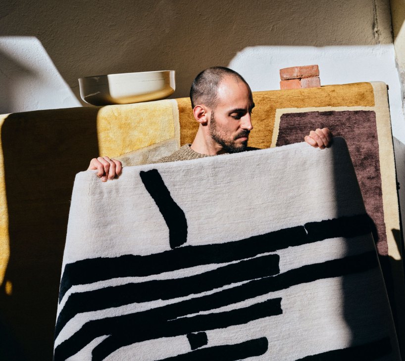 Man examining textile with black and white striped pattern in workshop surrounded by colorful fabric samples