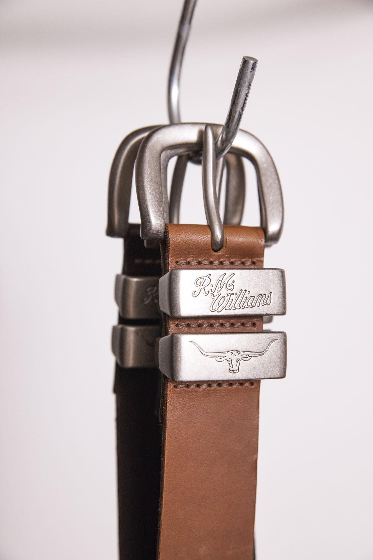 Close-up of brown leather belt with metal buckle featuring RM Williams branding and longhorn cattle logo