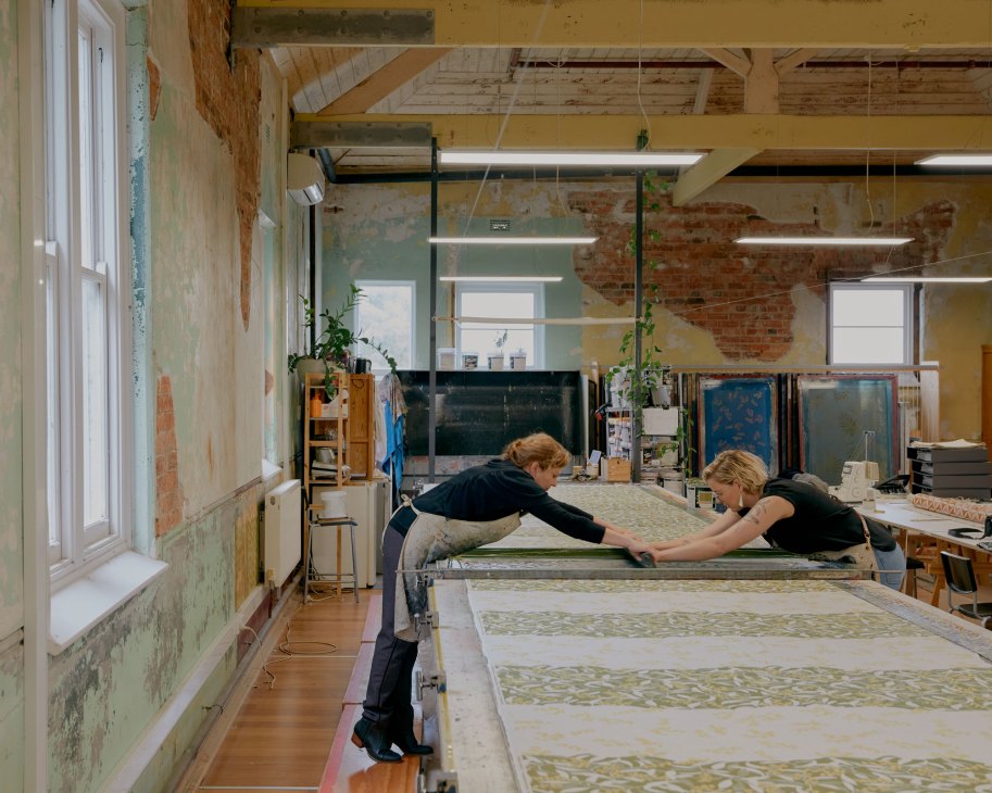Two artists working on large-scale printmaking project in converted studio space with exposed brick walls