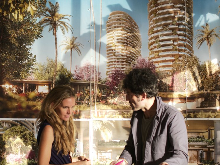 Two people examining an architectural model of modern high-rise towers with tropical landscaping in a presentation room