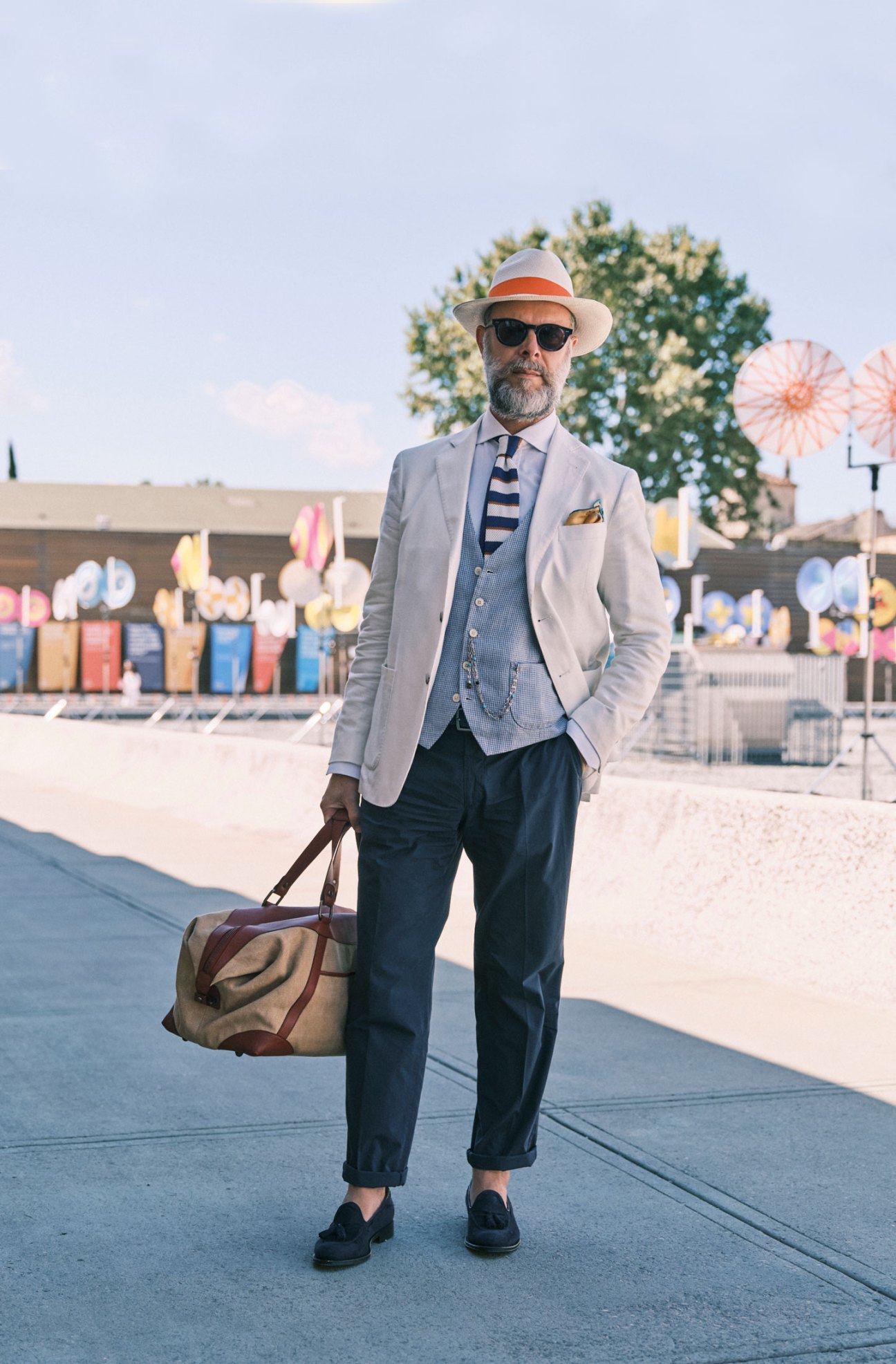 Man in patterned blazer carrying leather bag in outdoor urban setting