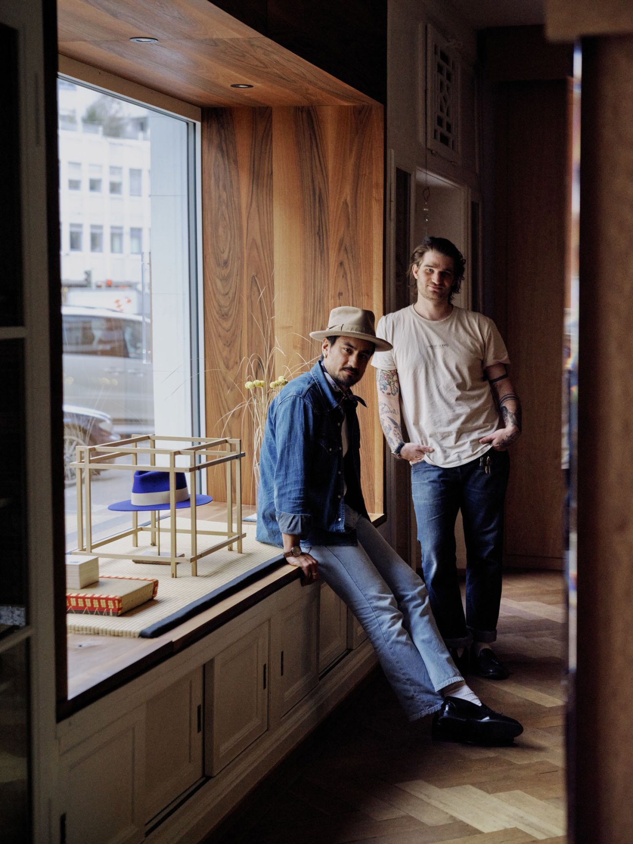 Two men in a minimalist studio with wooden furniture and large windows displaying Onkai Heiwa accessories.