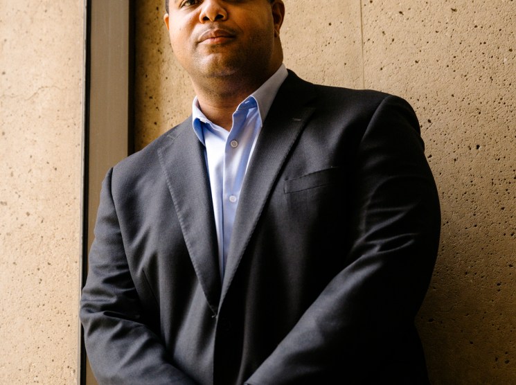 Dallas Mayor Eric Johnson in a dark suit and blue shirt standing against a concrete wall