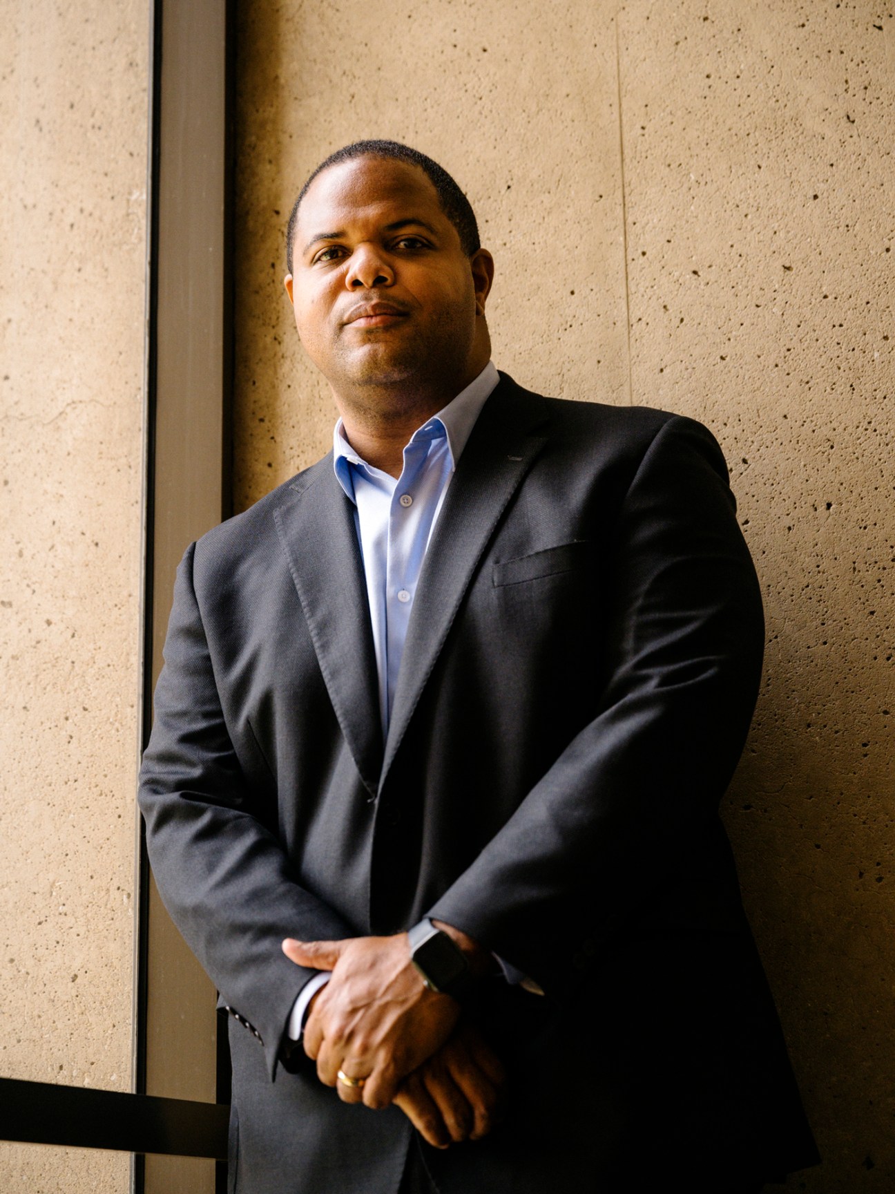 Dallas Mayor Eric Johnson in a dark suit and blue shirt standing against a concrete wall