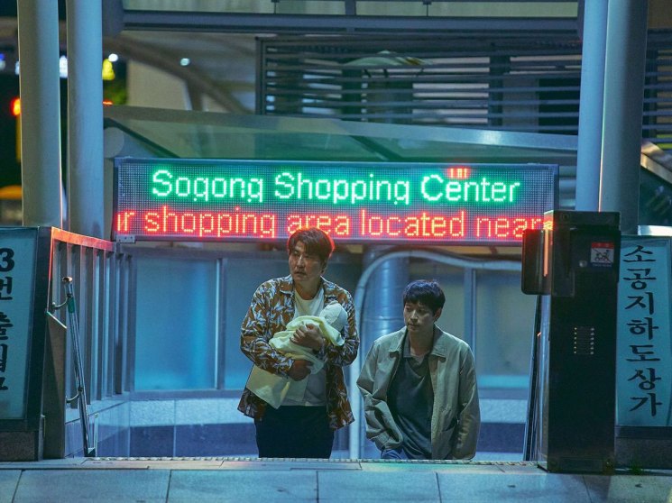 Two men emerging from a subway station entrance with Korean signage and digital displays