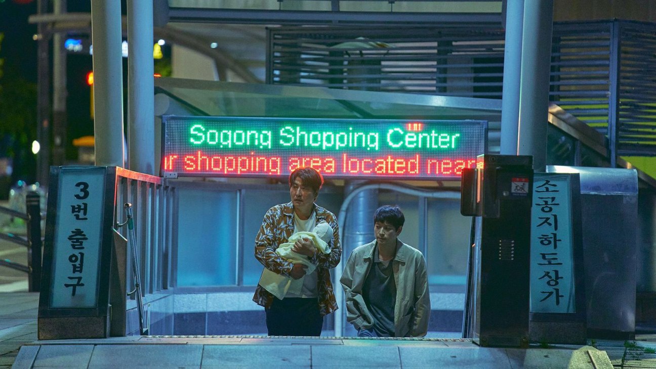 Two men emerging from a subway station entrance with Korean signage and digital displays