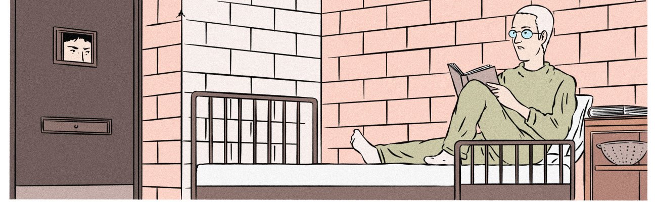 Man in green clothing reading a book while sitting on a bed in a sparse room with brick walls