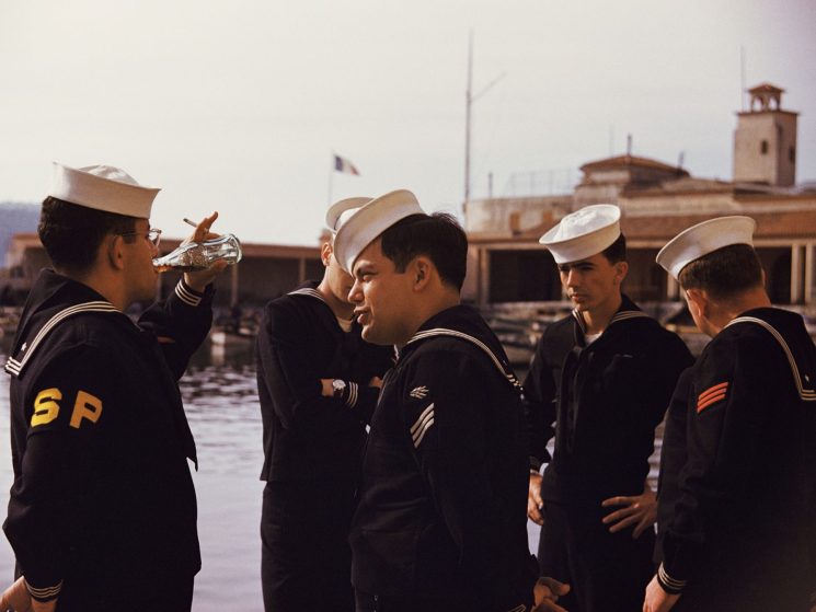 Five US sailors in naval uniforms standing at a harbor in Marseille, one drinking from a bottle