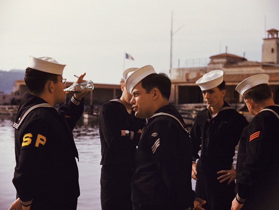 Five US sailors in naval uniforms standing at a harbor in Marseille, one drinking from a bottle