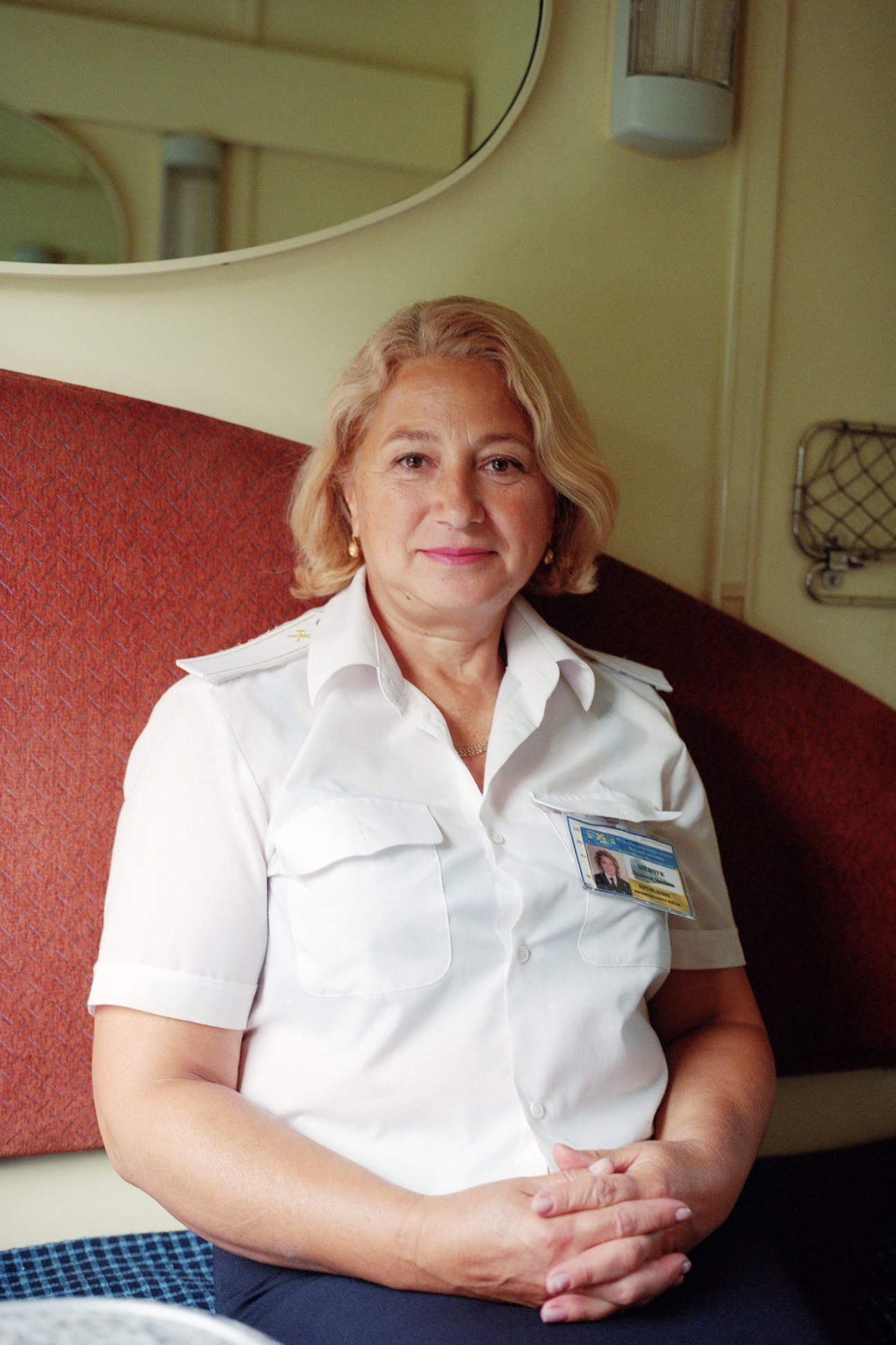 Railway attendant Lyudmyla Shevchuk sits in a train compartment wearing a white uniform and name badge