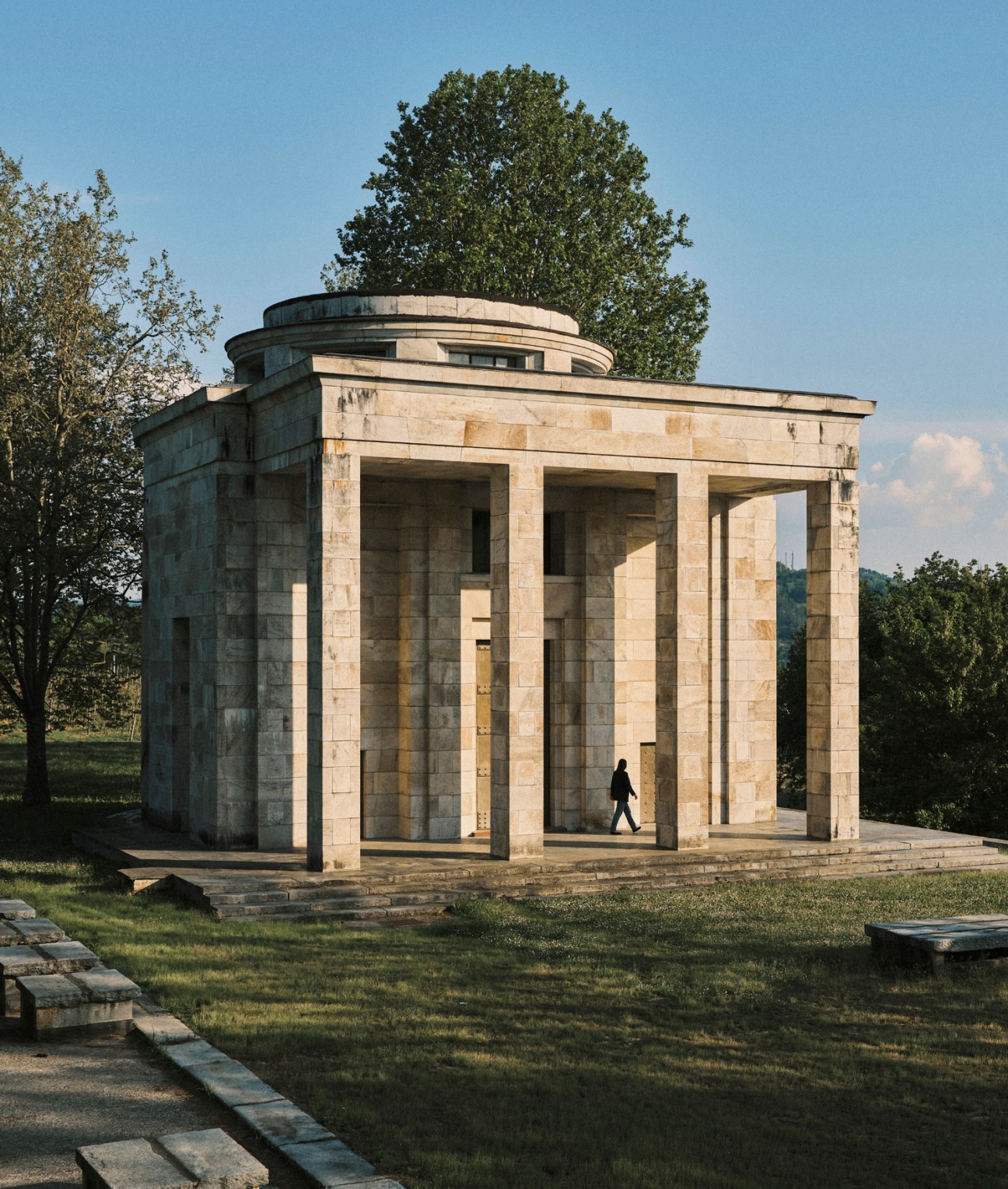 Classical stone mausoleum with columns and cylindrical structure set in parkland with trees