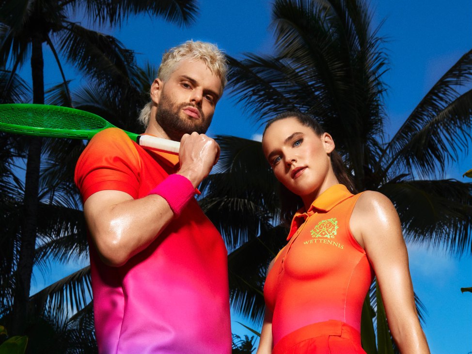 Sofi Tukker duo posing with tennis racket against tropical palm tree backdrop in colorful athletic wear