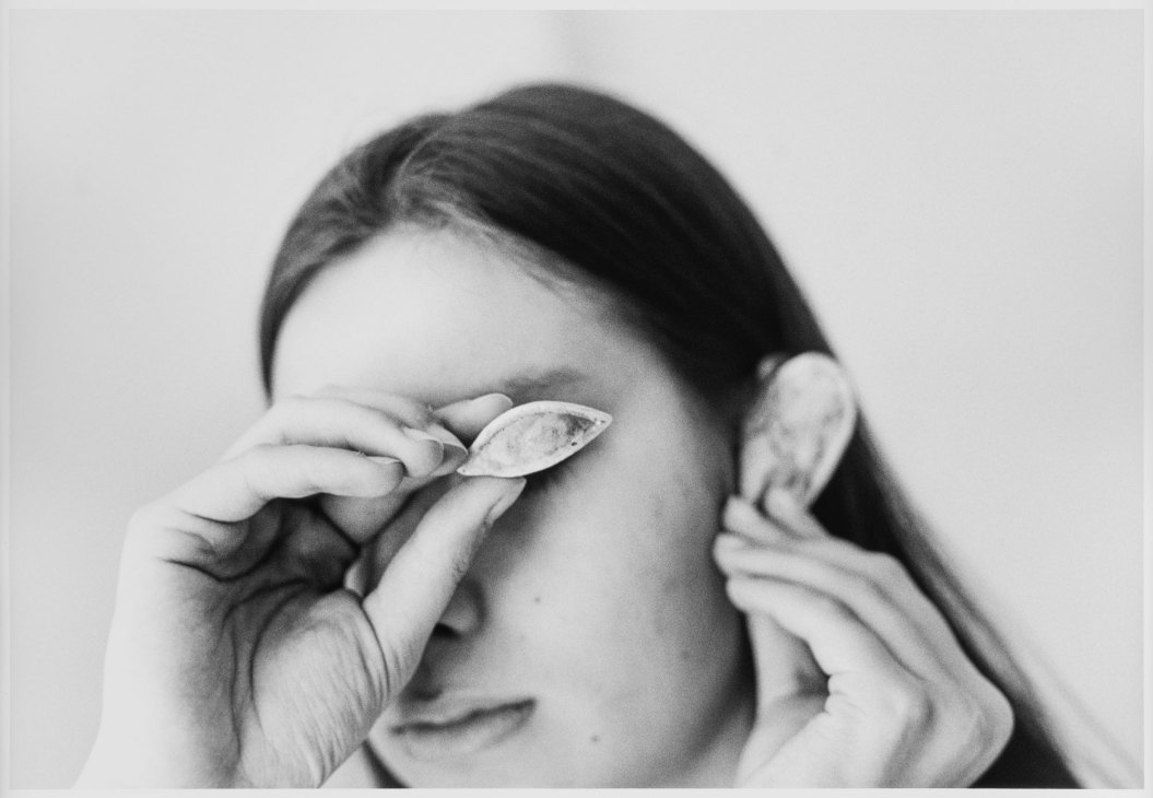 Black and white photograph showing a person holding what appears to be a shell or organic object over their eye