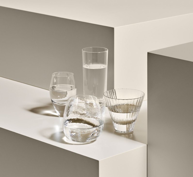 Collection of clear glass vessels and drinking glasses filled with water displayed on white stepped platforms
