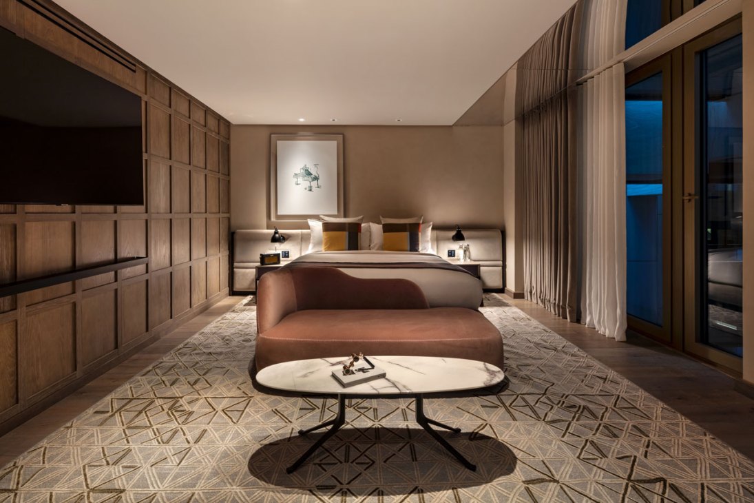 Elegant hotel bedroom with warm wood paneling, earth-toned bedding, and contemporary furnishings