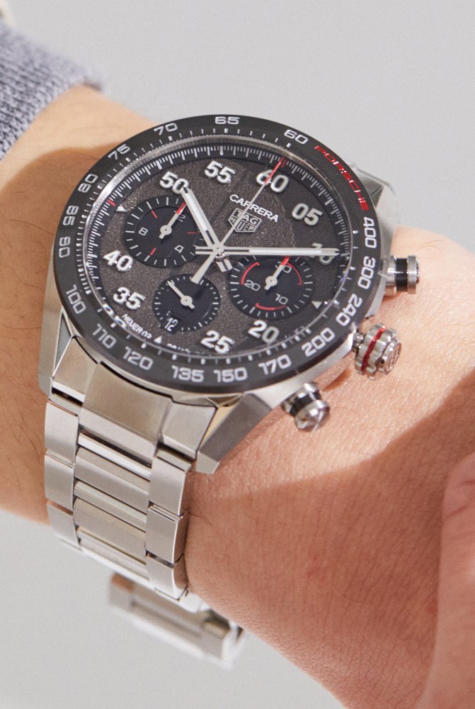 TAG Heuer Carrera Porsche chronograph watch with black dial on wrist wearing grey knit sweater