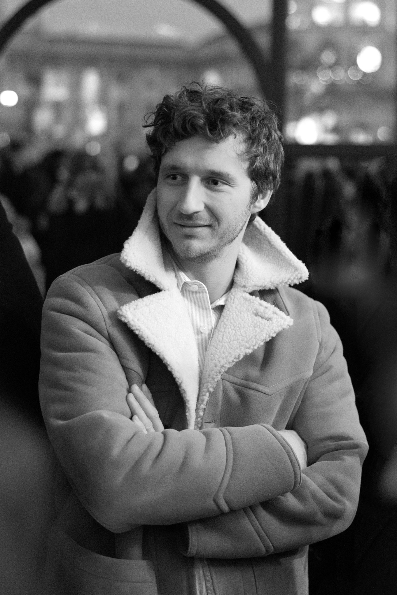 Man in shearling jacket with arms crossed standing outdoors in black and white portrait