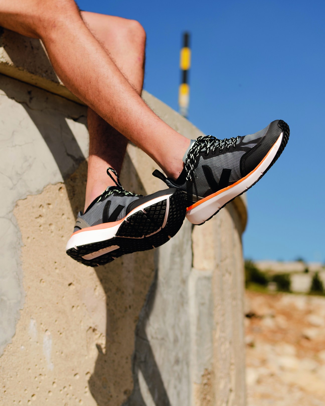 Person wearing Veja Marlin running shoes with grey, black and orange colorway on concrete ledge