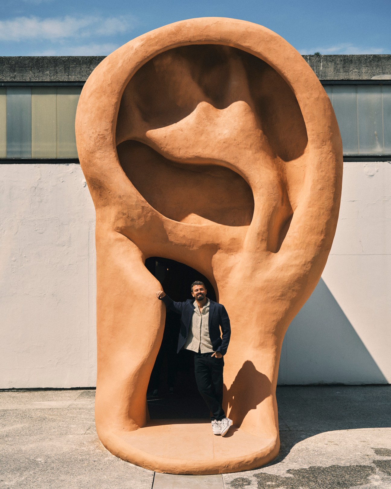Man standing inside large terracotta ear sculpture at Venice Biennale, Brazilian artist Jonathas de Andrade's installation.