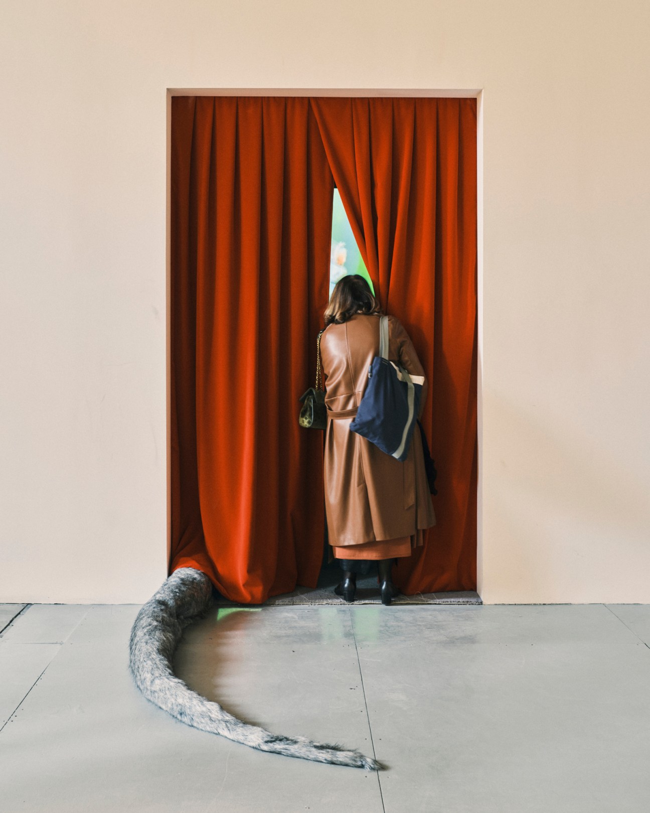 Woman from behind peeking through red curtains at Venice Biennale Arsenale with sculptural tail-like element on floor