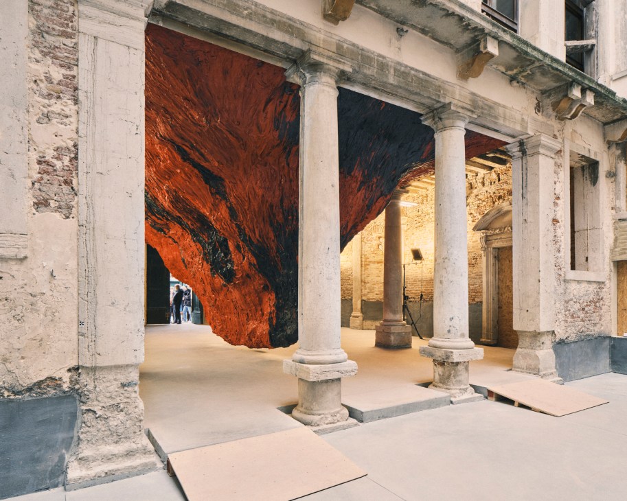 Large red-orange abstract artwork displayed in classical stone gallery with columns and arched ceiling.
