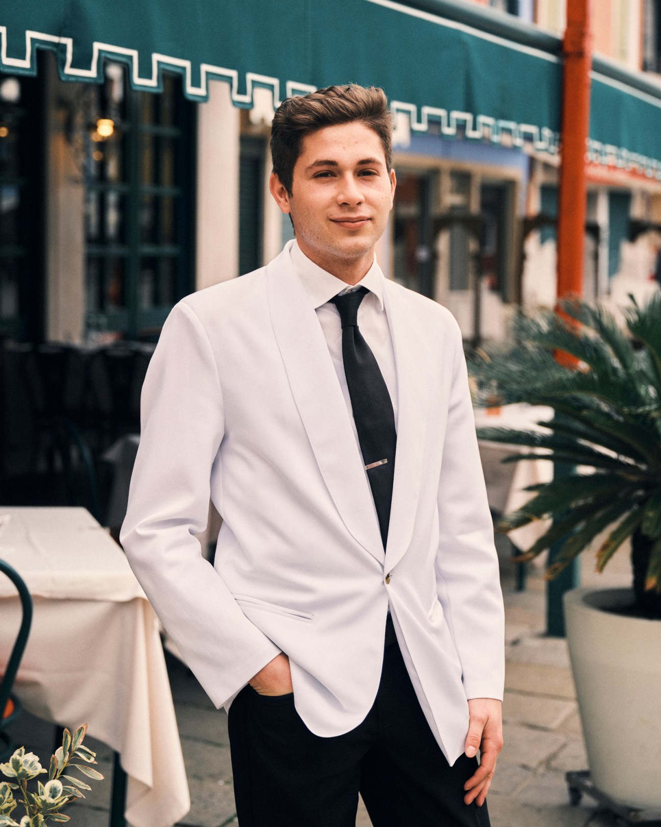 Young man in light colored suit jacket and dark tie smiling outdoors on a street