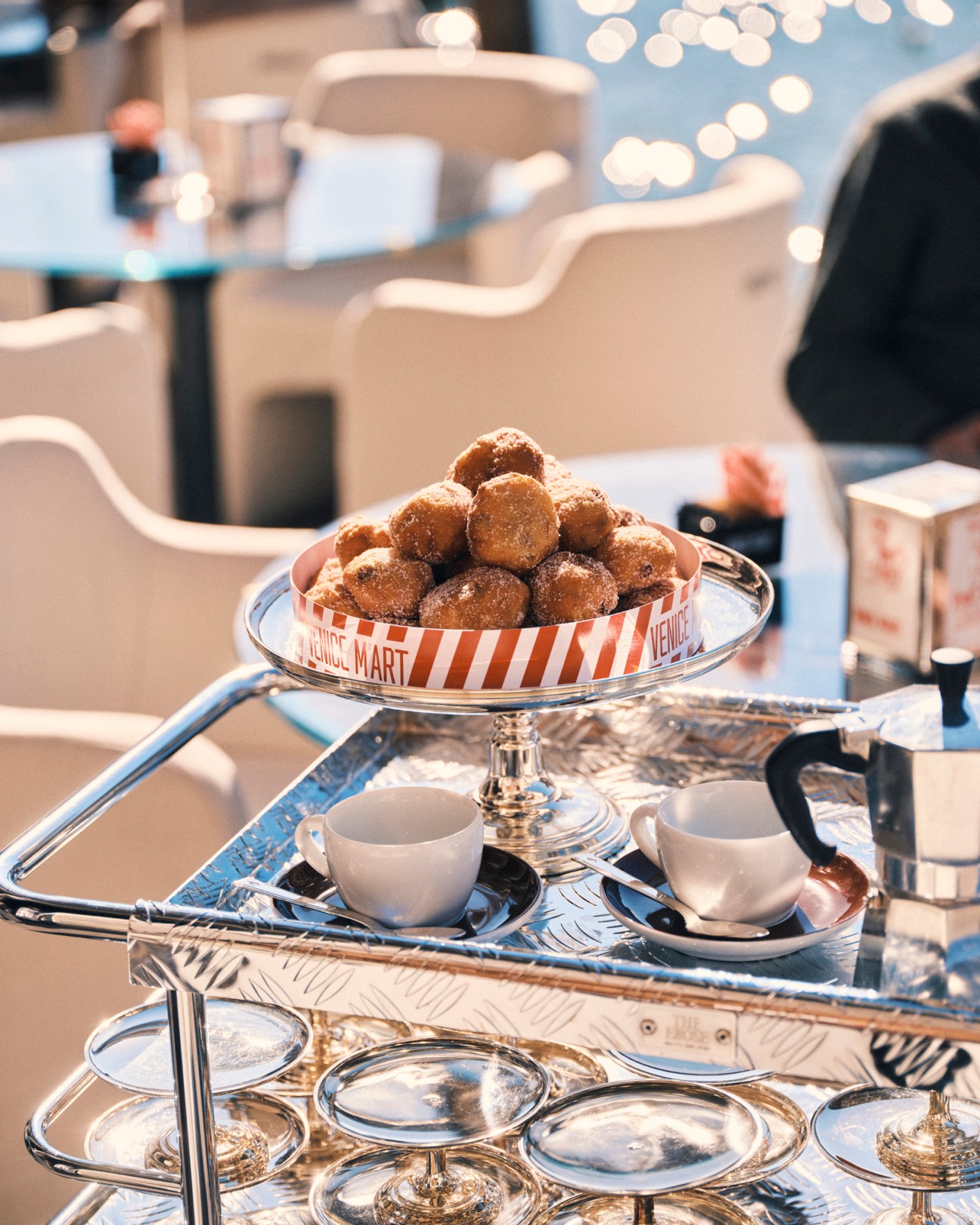 Traditional Venetian frittelle pastries arranged on an elegant tiered serving stand with coffee cups