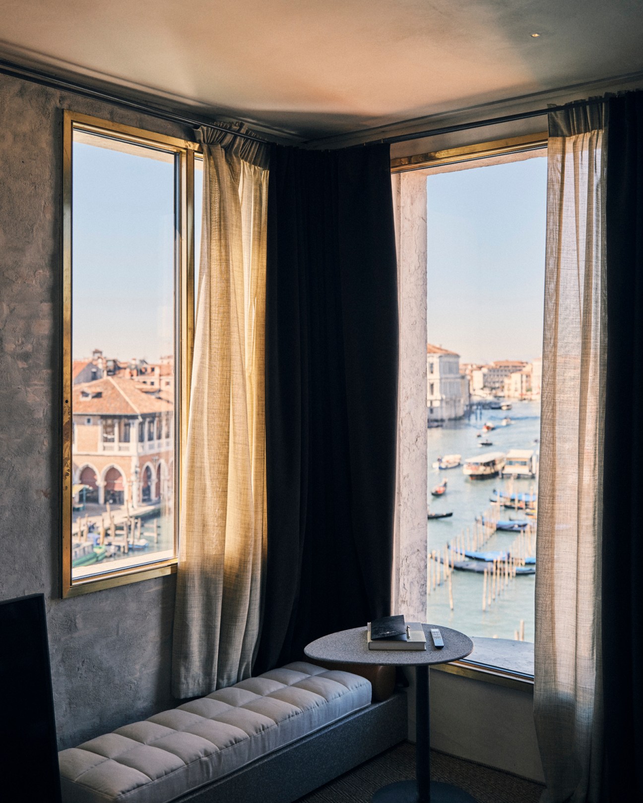 Hotel room interior with large windows overlooking Venice canal, featuring modern seating and small table