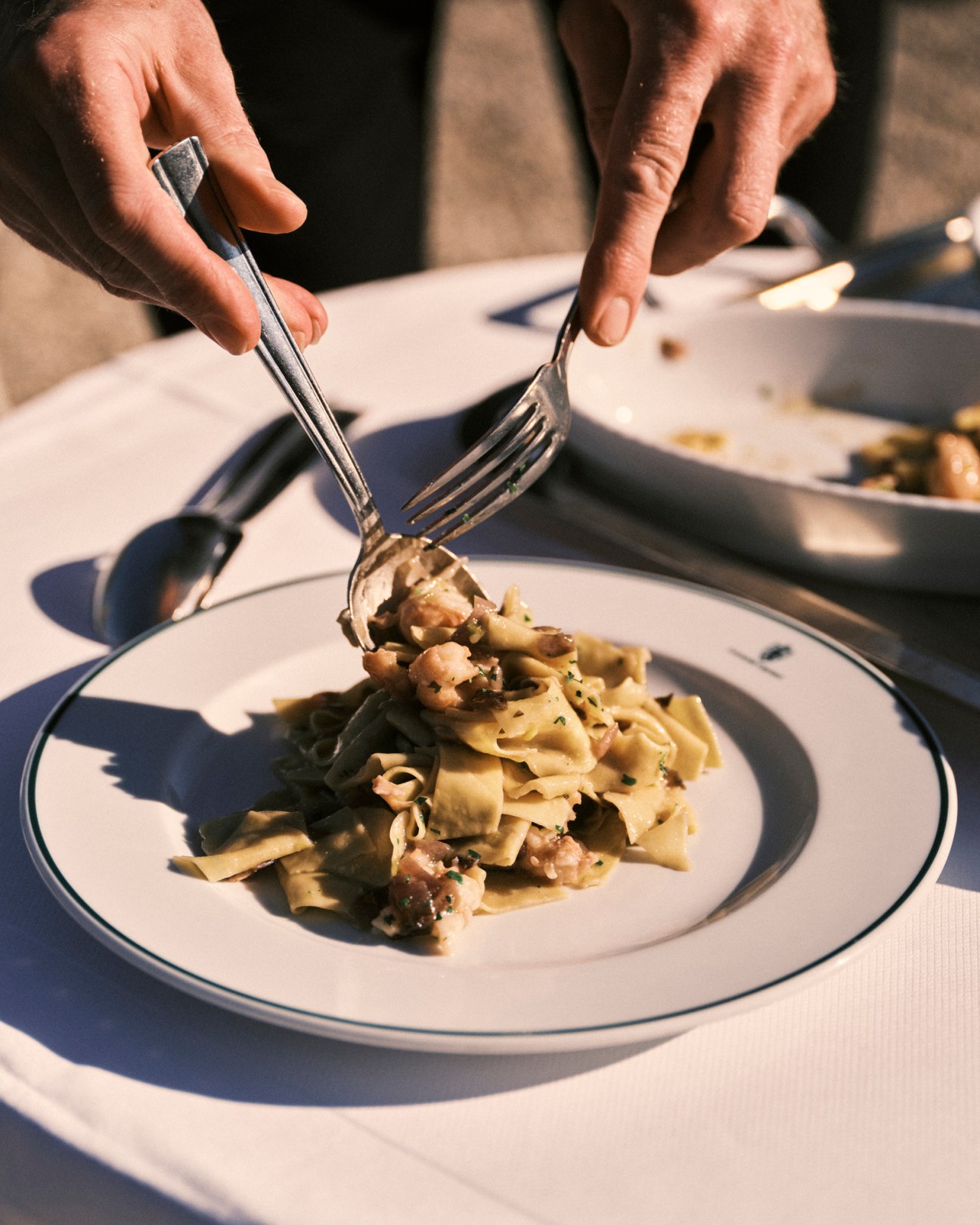 Hands using knife and fork to cut pasta dish with mushrooms and herbs on white plate