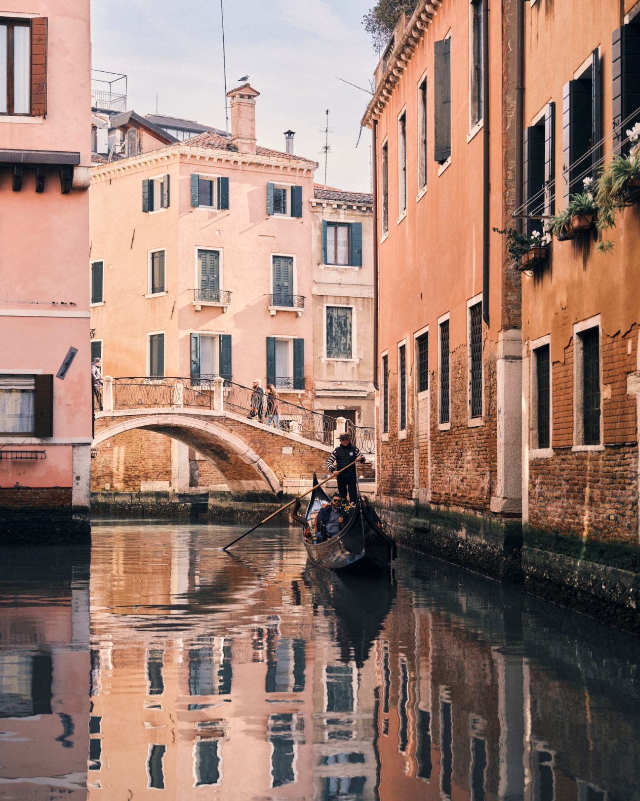Gondolier in traditional striped shirt navigating a narrow Venice canal lined with historic buildings