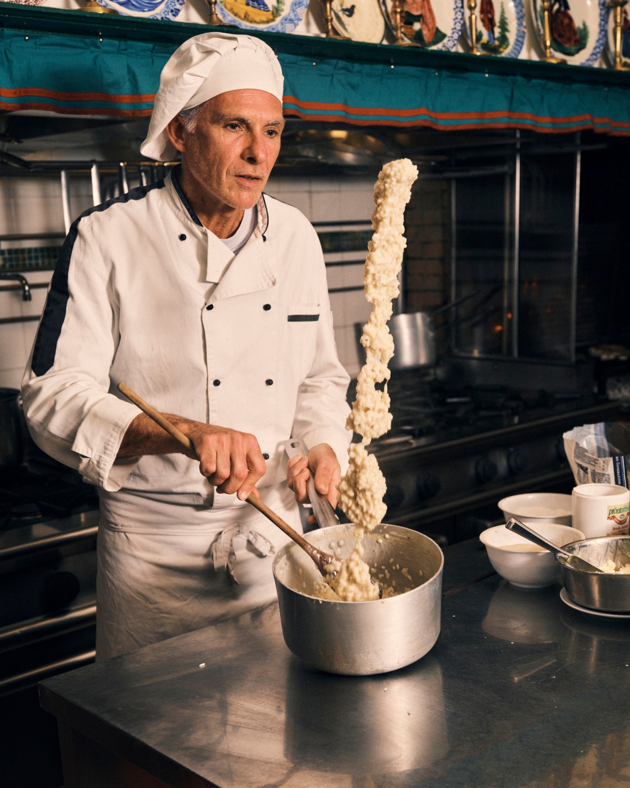 Chef in white uniform and hat preparing risotto with long wooden spoon in restaurant kitchen
