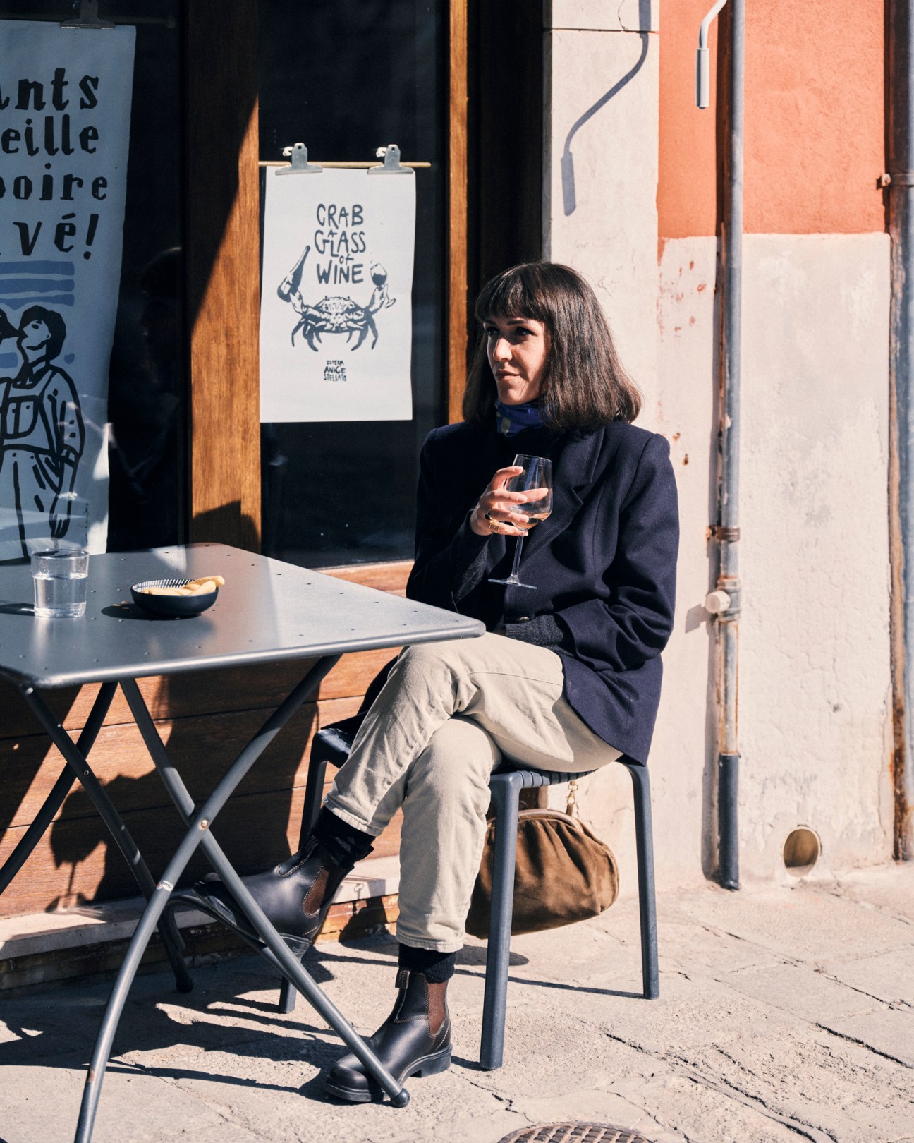 Woman in dark blazer sitting at outdoor table holding wine glass in sunny Venice setting