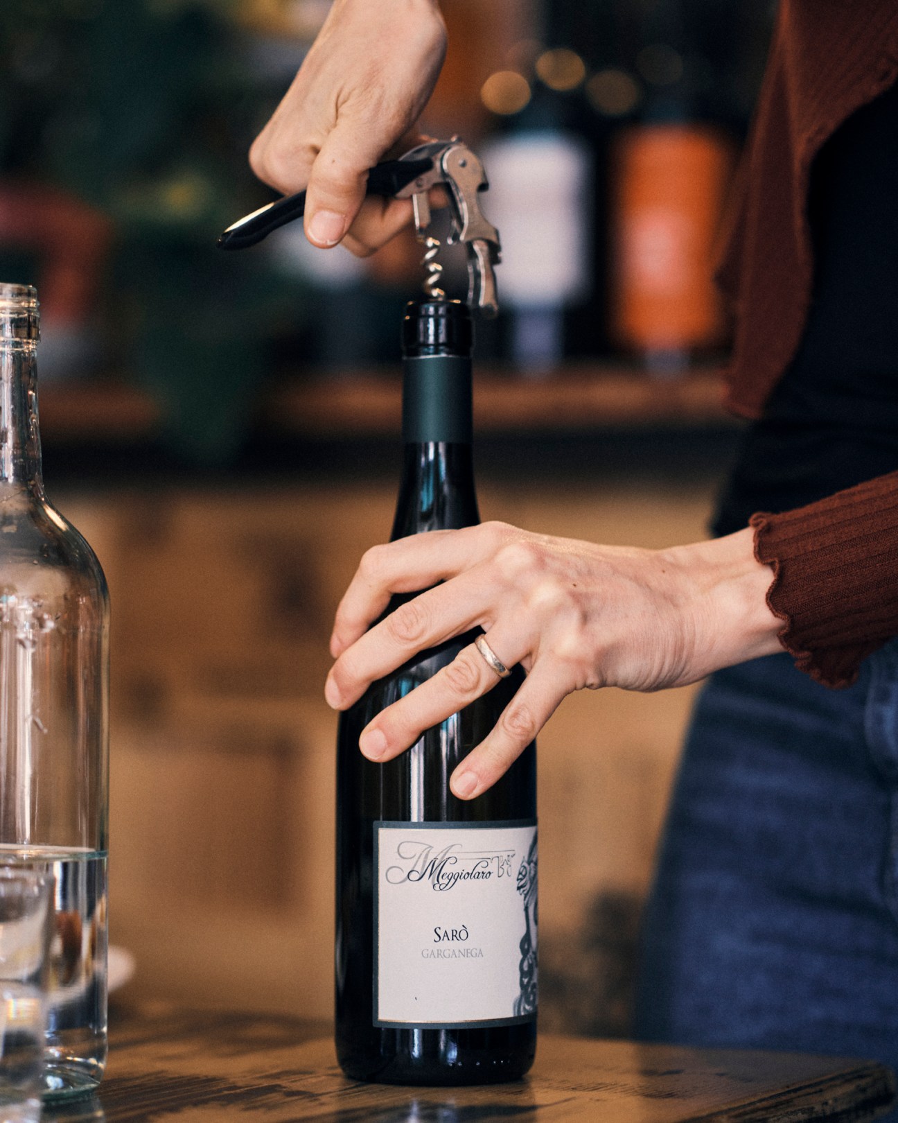Person opening a bottle of Sarò Gargamega wine with corkscrew at a table