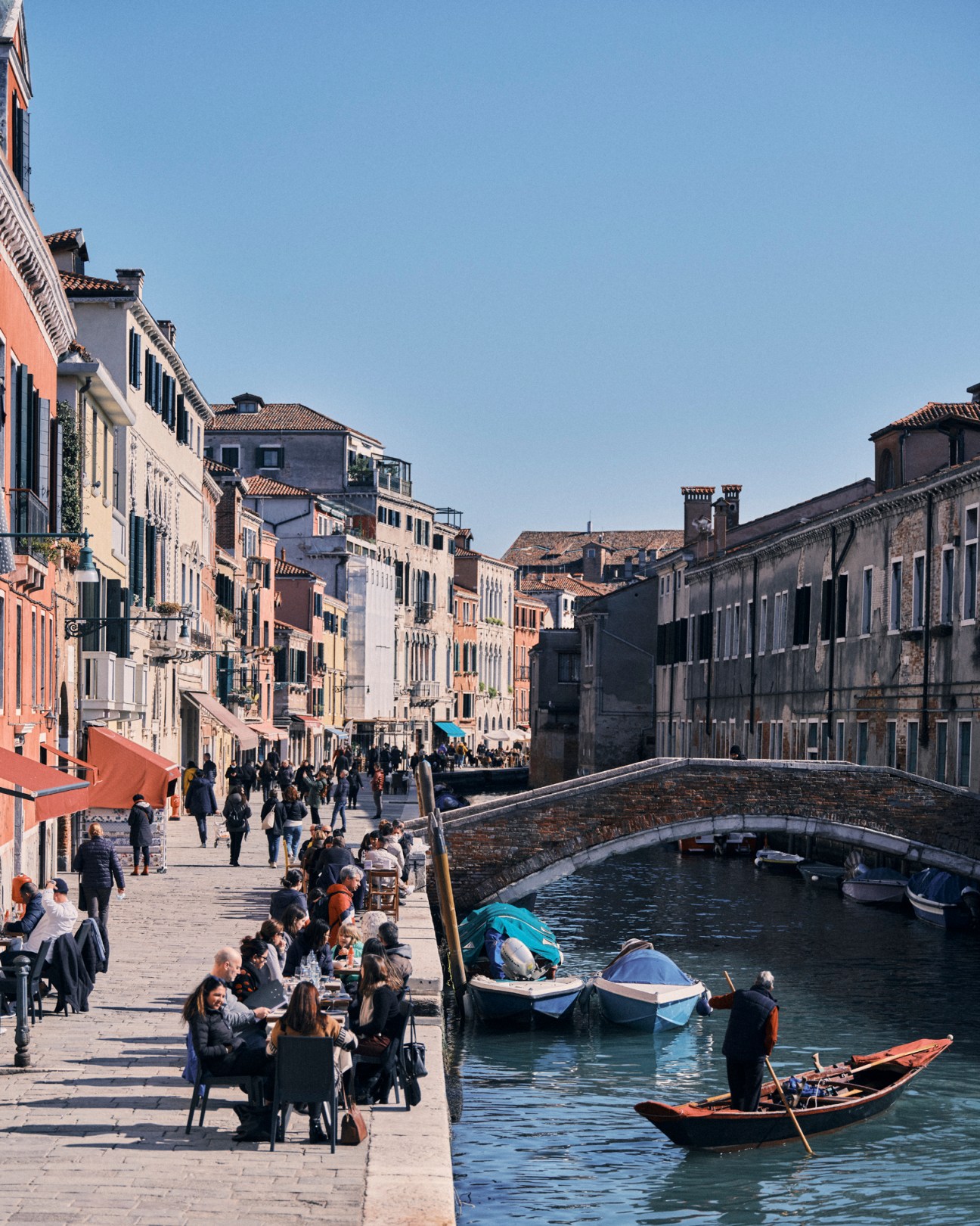 Cannaregio district waterfront with people dining at outdoor tables along canal with boats and historic buildings