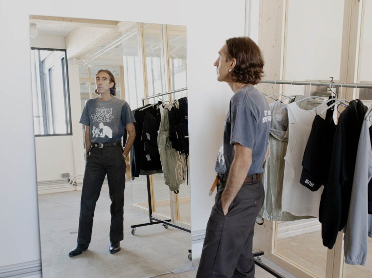 Brice Partouche looking in mirror while wearing gray t-shirt in clothing showroom