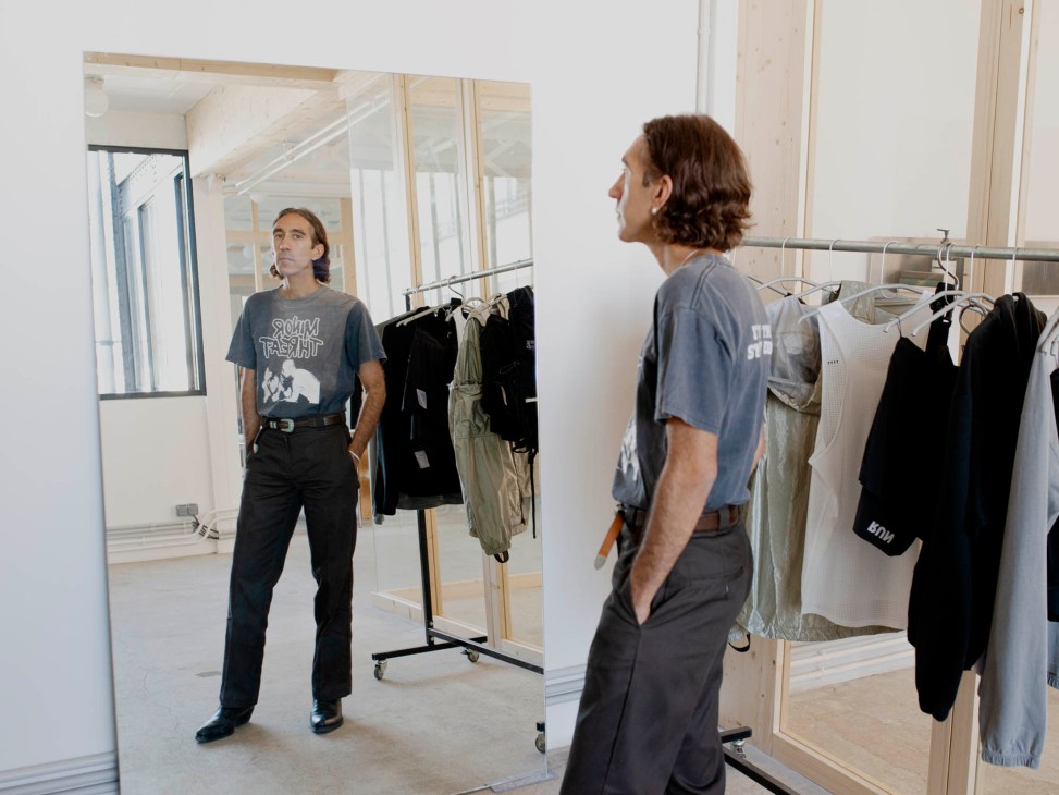 Brice Partouche looking in mirror while wearing gray t-shirt in clothing showroom
