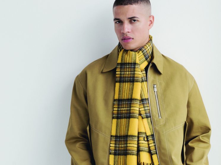 Model wearing olive-green Hermès jacket with yellow tartan scarf, cream APC jumper and beige De Bonne Facture trousers.
