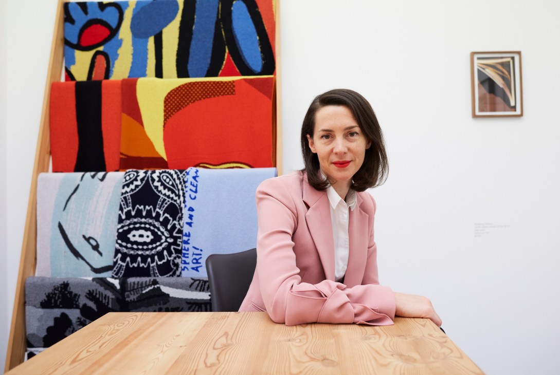 Nanna Hjortenberg, director of Chart Art Fair, sitting at wooden table in pink blazer with colorful artwork behind